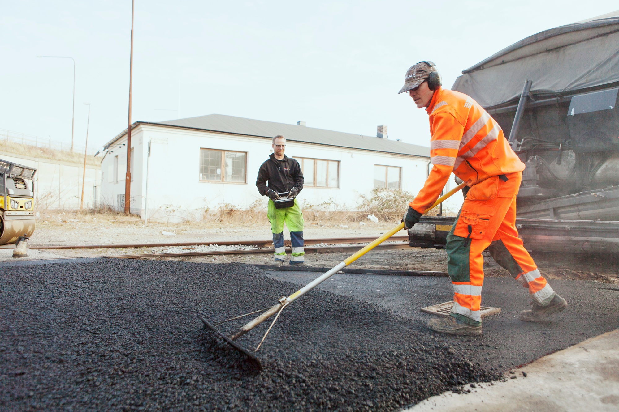 Full length of manual worker with rake spreading asphalt on street