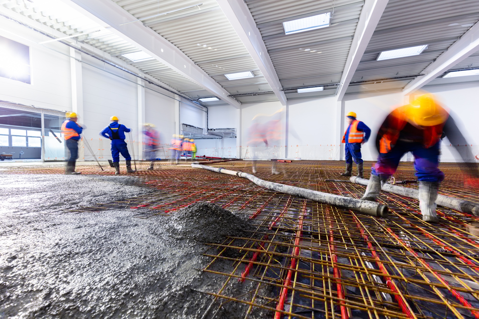 Workers do concrete screed on floor with heating in a new warehouse building